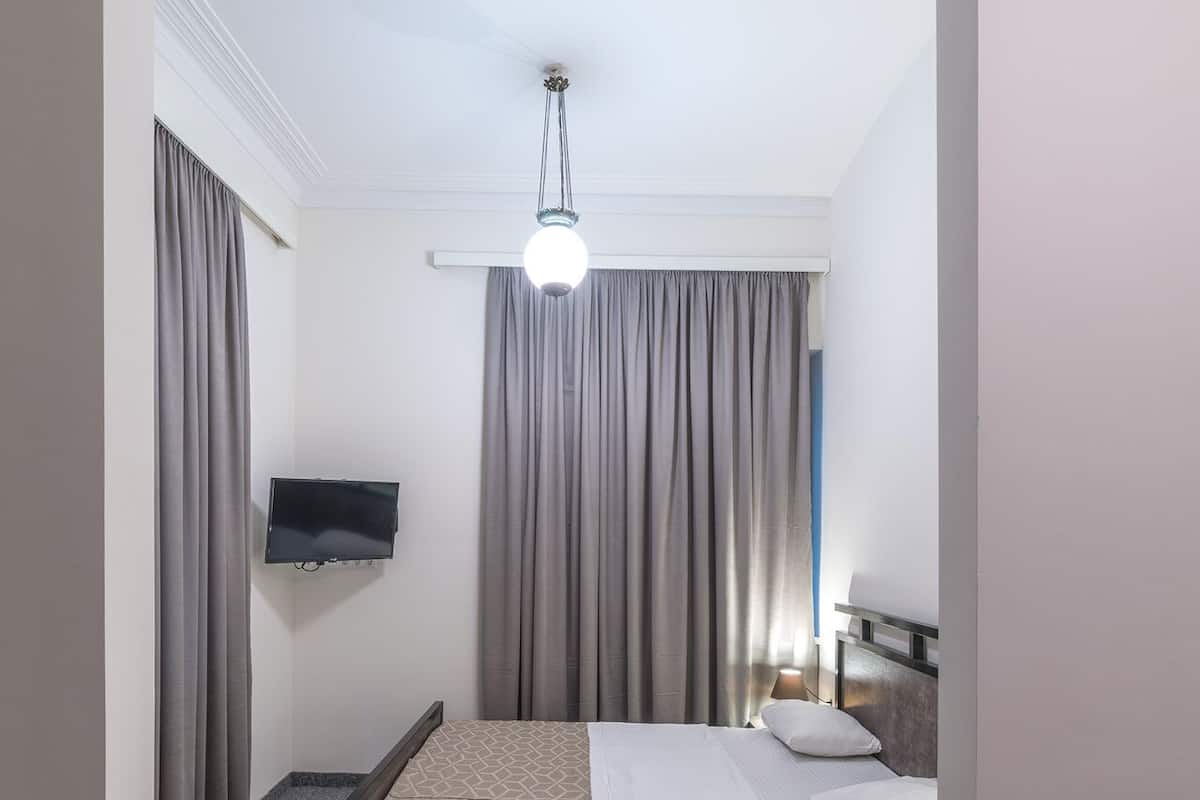 A hotel room with a bed, a flat-screen TV, a desk with a lamp, and a ceiling light.