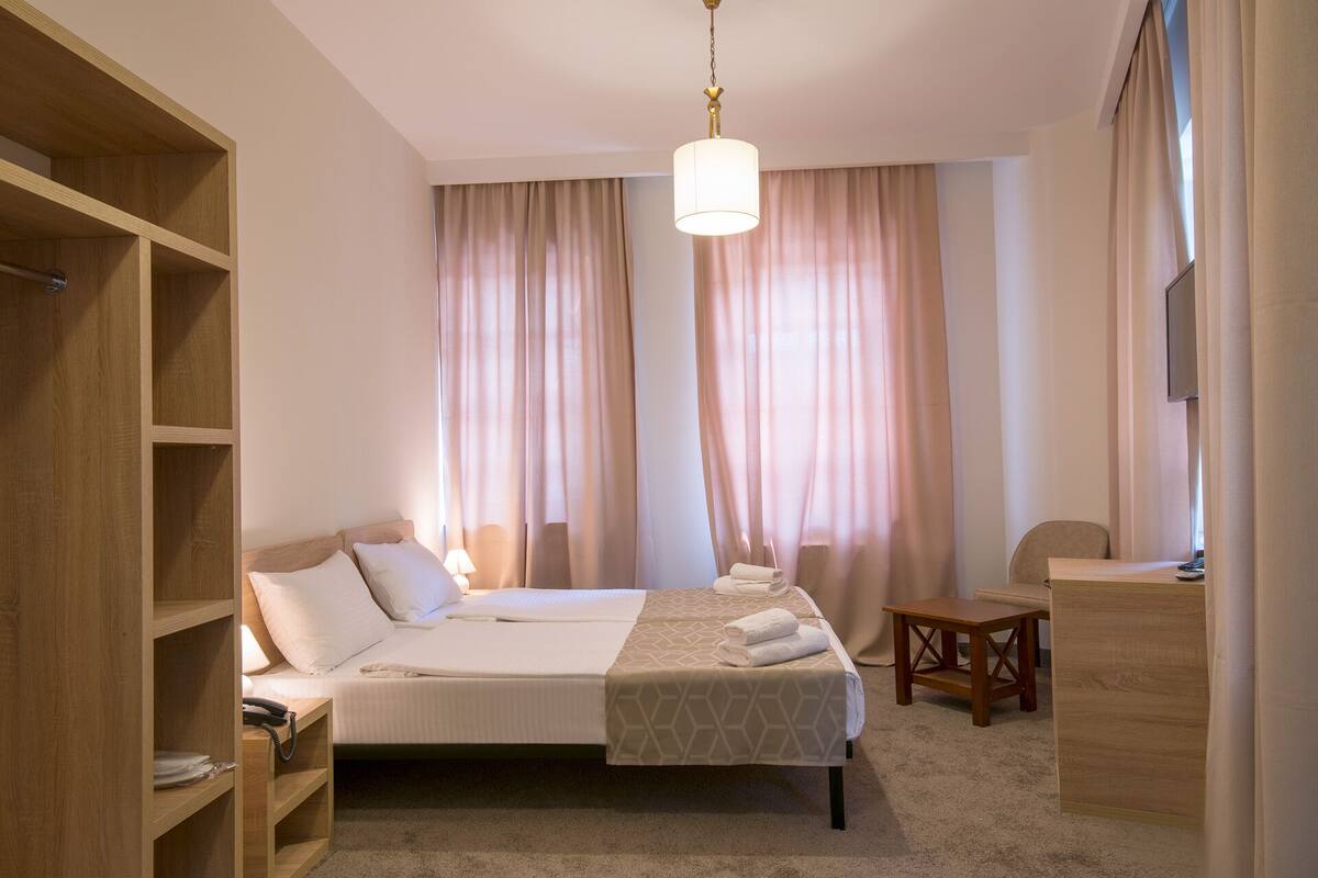 A hotel room with a bed, bedside tables, a desk, a chair, and a wardrobe.