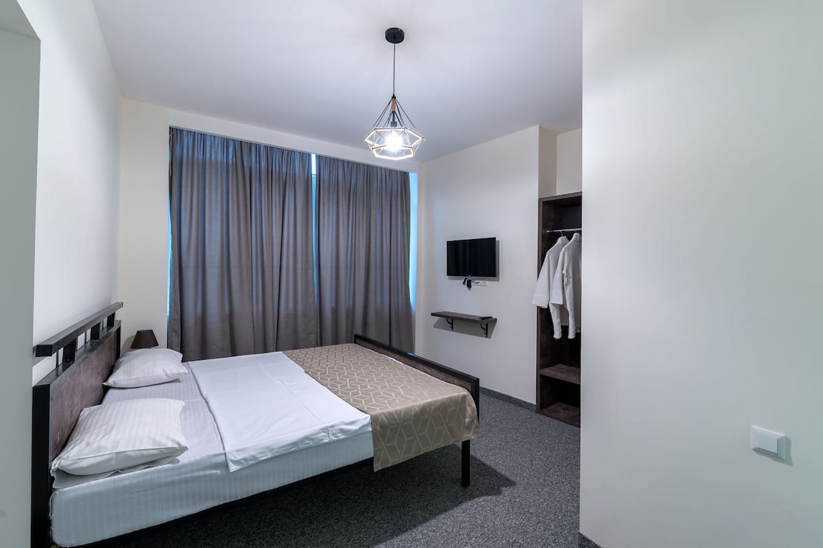 A modern hotel room with a bed, a TV mounted on the wall, and a wardrobe.