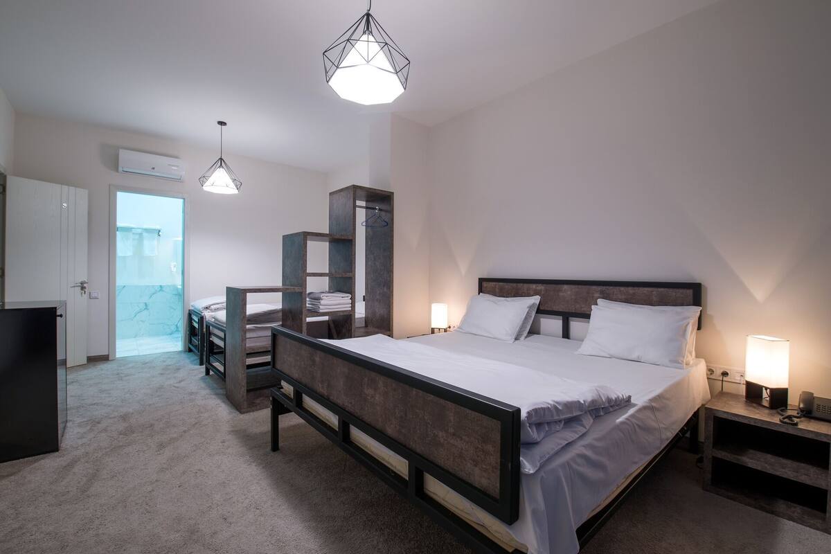 A bedroom with a large bed, bedside tables, a wardrobe, and a hanging light fixture.