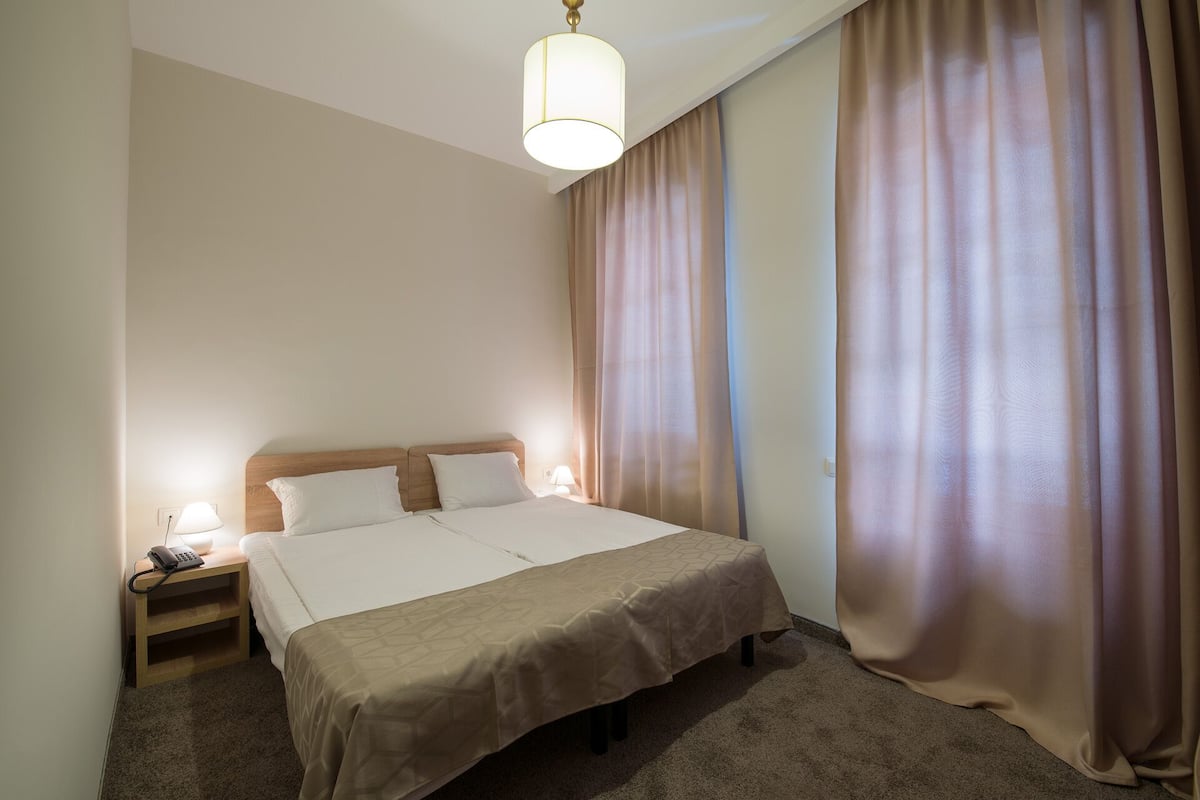 A hotel room with a large bed, two bedside lamps, a nightstand with a phone, and a hanging light fixture.