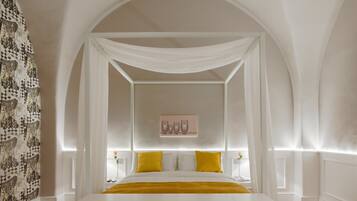 Quarto com cama de dossel, paredes brancas e papel de parede estampado em uma das paredes.