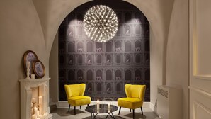 A room with a fireplace, two yellow chairs, a round table, and a decorative ceiling light. - Quattro Canti Suites (Catania)