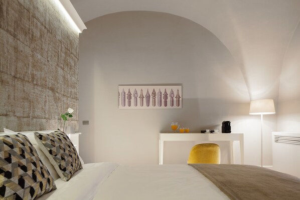 A modern hotel room with a large bed, a white desk, a yellow chair, and a wall-mounted artwork. - Quattro Canti Suites (Catania)