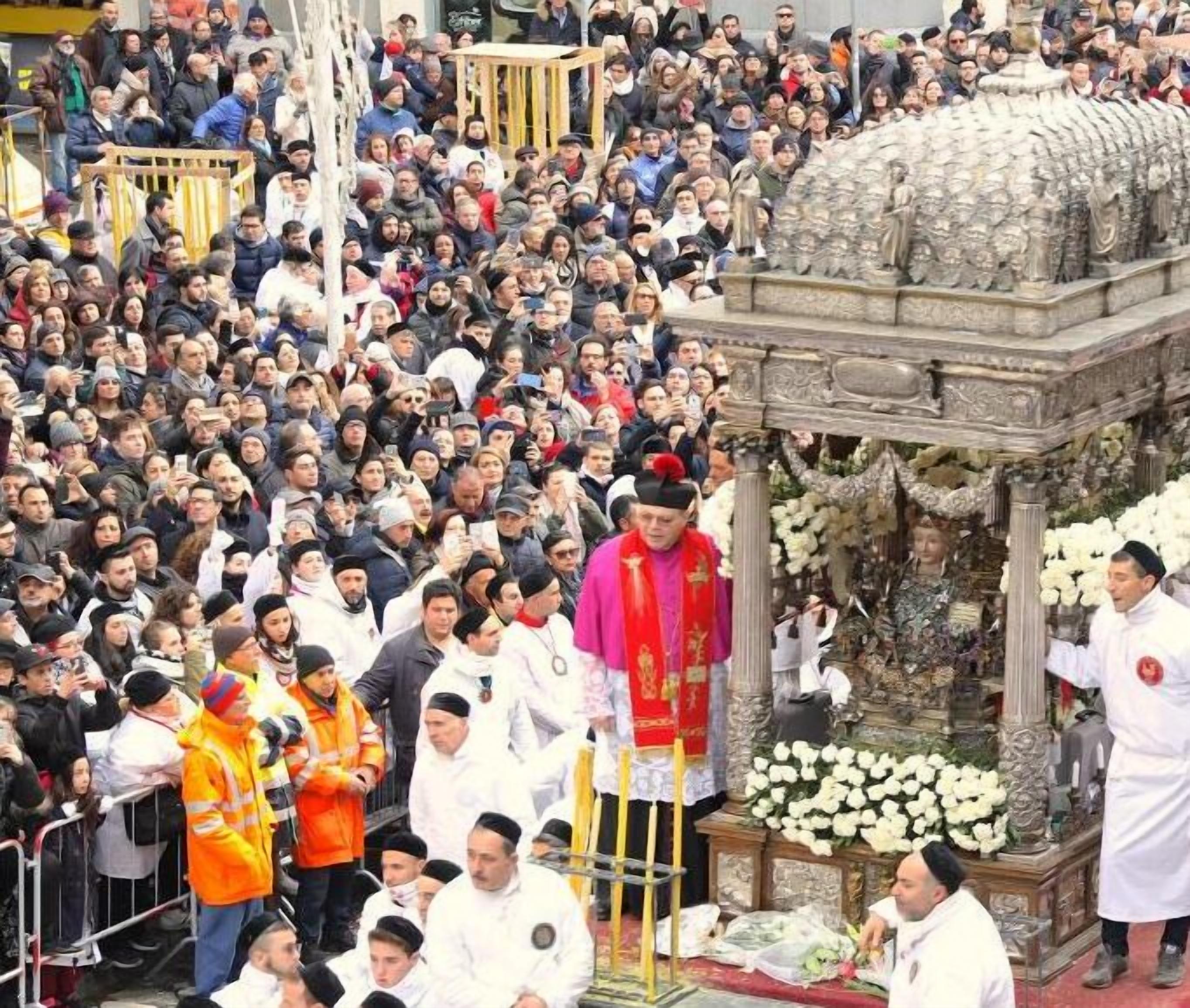 A crowded outdoor event with a central structure adorned with flowers and statues.