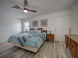 A bedroom with a bed, a nightstand, a dresser, a ceiling fan, and a door.