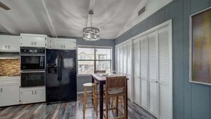 Een keuken met witte kastjes, een zwarte koelkast en een eethoek met een houten tafel en stoelen.