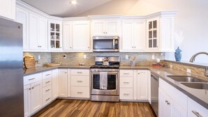 A modern kitchen with white cabinetry, a stainless steel refrigerator, a built-in microwave, and a stove. - Gorgeous Ocean View Twinhome w/AC! (Encinitas)