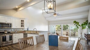 A spacious kitchen with white cabinets, a large island, and a dining area with wooden furniture. - Gorgeous Ocean View Twinhome w/AC! (Encinitas)