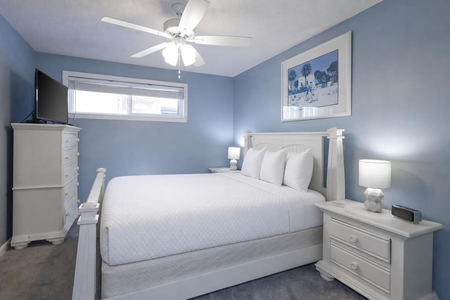 Une chambre à coucher comprenant un lit, des tables de chevet, une commode, un ventilateur de plafond et une fenêtre.