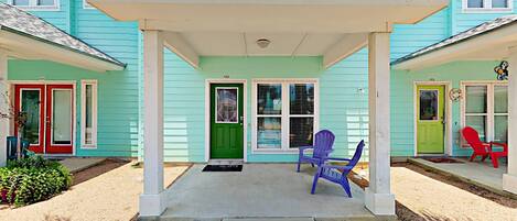 Une maison à deux étages avec un porche couvert, des portes numérotées et des chaises d’extérieur.
