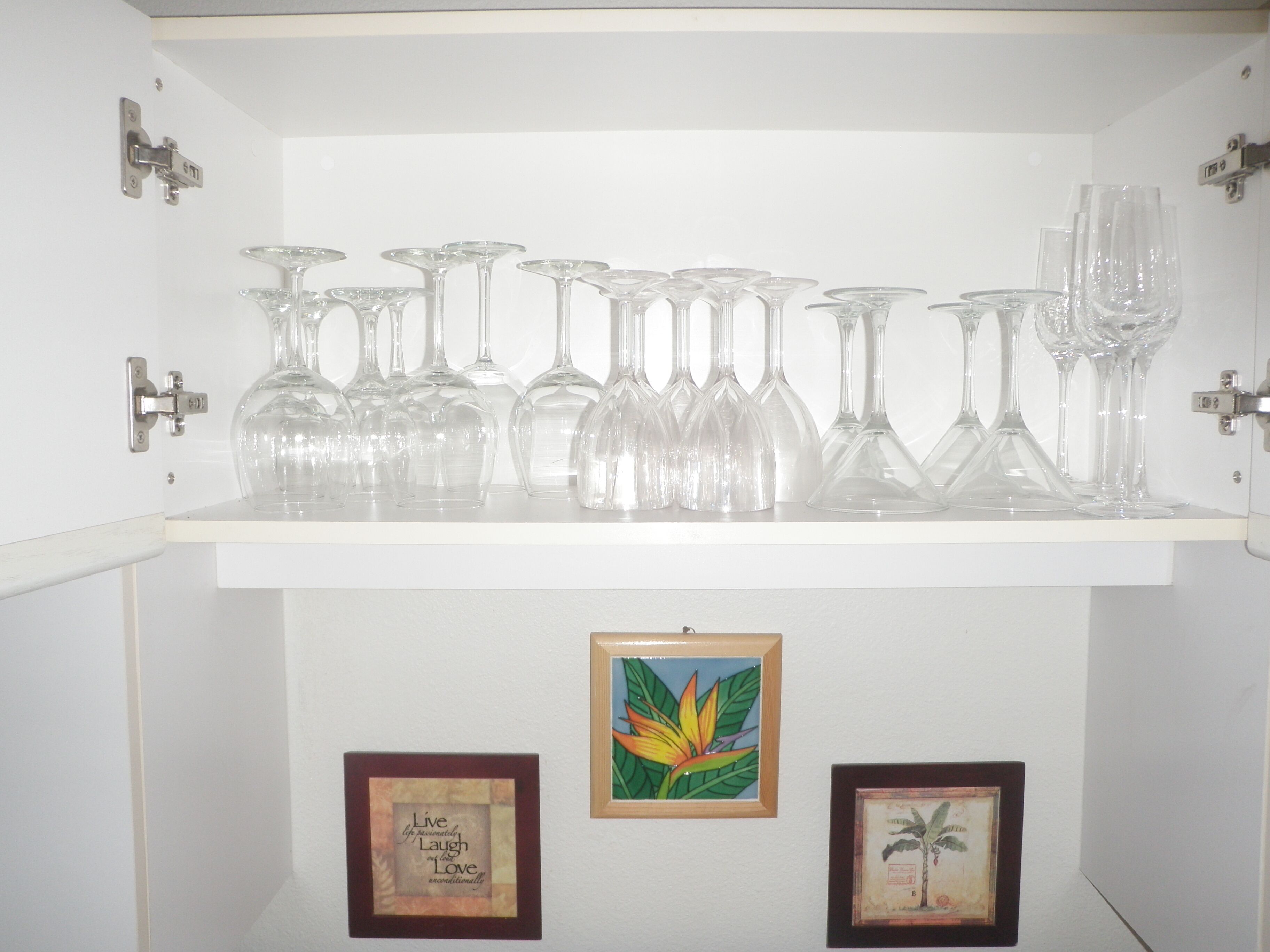 A shelf with various clear glassware and two framed pictures on a white wall.