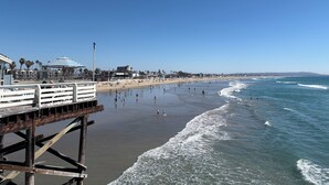Una playa con un muelle de madera, sombrillas y un cielo azul despejado.