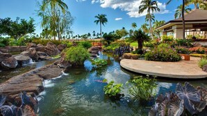 Un bassin à carpes koï agrémenté de rochers et de plantes tropicales, entouré d’un jardin aménagé avec des palmiers et un kiosque.