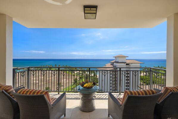 Un balcón con muebles de mimbre, un frutero y vista al océano y la playa.