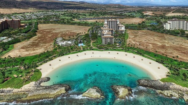 Vue aérienne d’un complexe hôtelier doté d’une grande plage en forme de croissant, de nombreux immeubles de grande hauteur et d’espaces paysagers environnants.