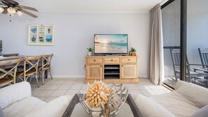 A living room with a TV, wooden cabinet, and a dining area with chairs and a table.