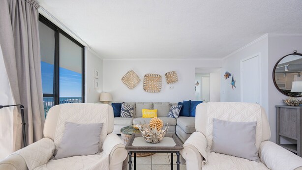 A living room with two white armchairs, a grey sofa with patterned cushions, and a coffee table with decorative items.