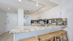A kitchen with white cabinets, a granite countertop, a stainless steel sink, and wooden bar stools.