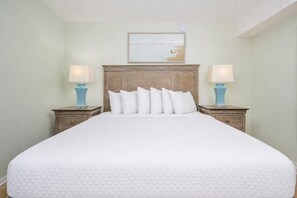 A large bed with a wooden headboard, two bedside tables with lamps, and a painting above the bed. - Phoenix 8 ~ 1 BR 1 BA ~ Top Floor AMAZING VIEWS!!! (Orange Beach)