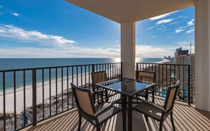 A balcony with a glass table and chairs, overlooking a beach and ocean.