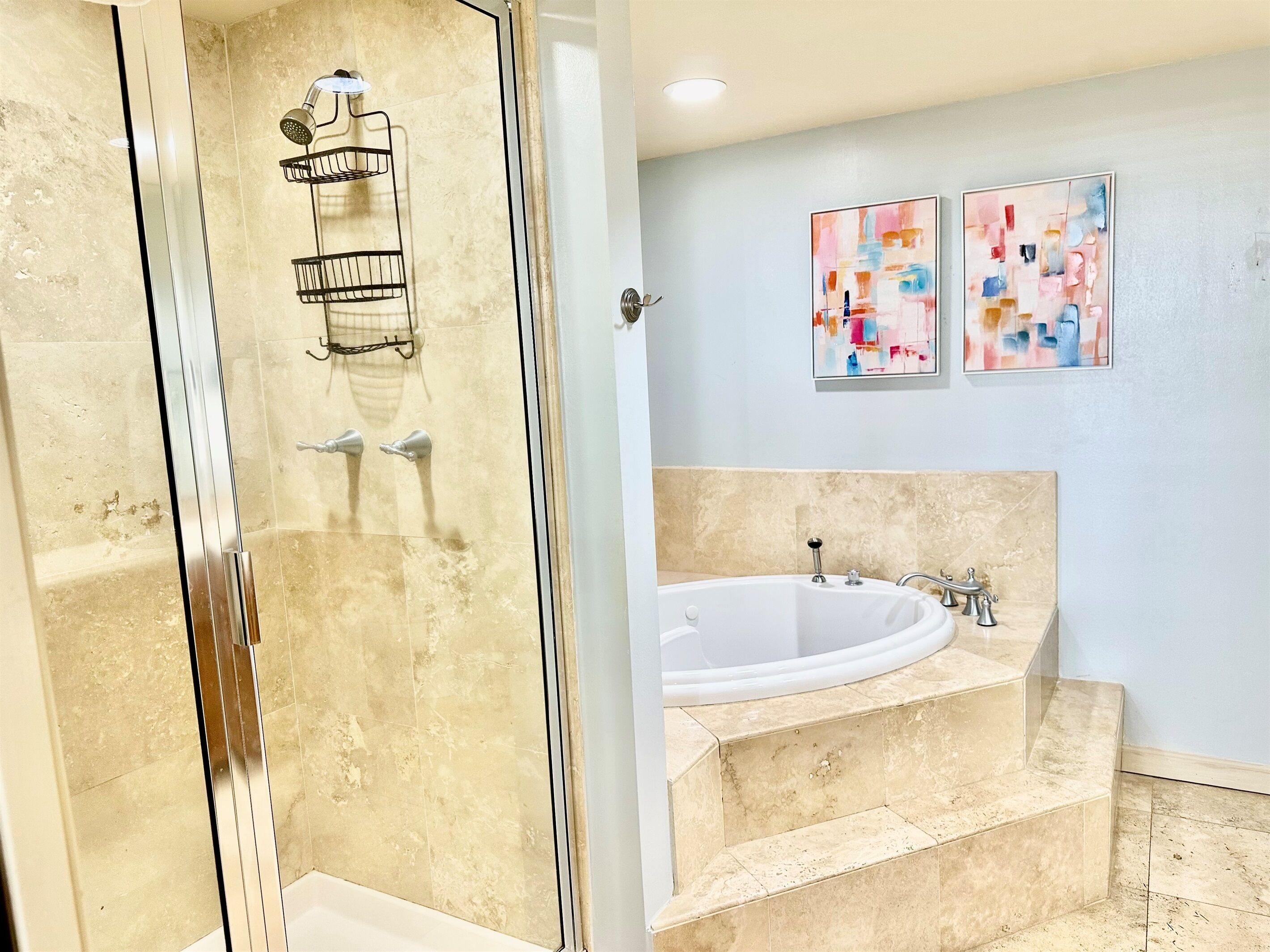 Une salle de bain dotée d’une douche à parois de verre, d’une baignoire sur pieds et de deux tableaux abstraits accrochés au mur.