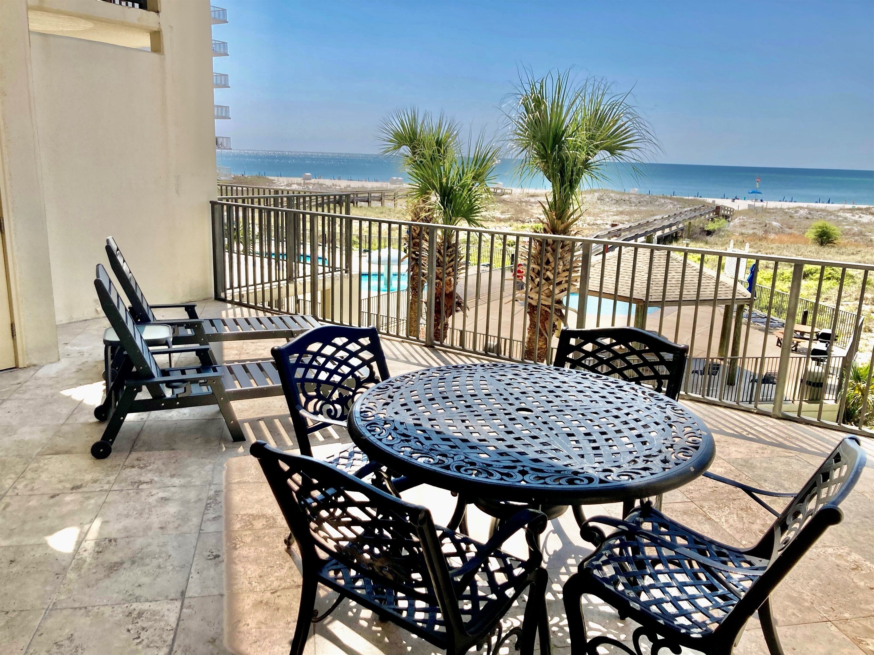 A balcony with a round table and chairs, overlooking a beach and a pool.