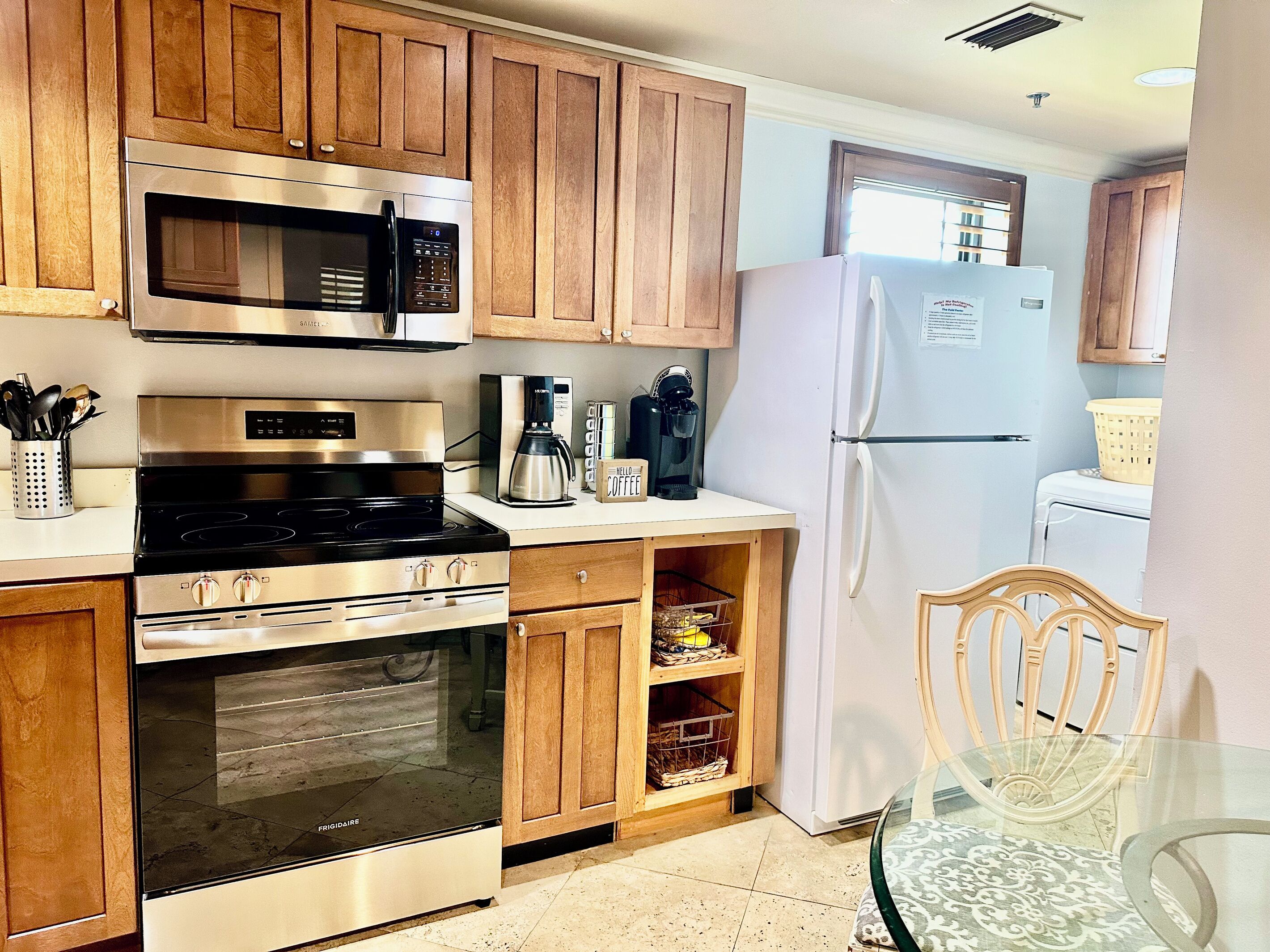 Una cocina con armarios de madera, electrodomésticos de acero inoxidable, una mesa de vidrio y un refrigerador.