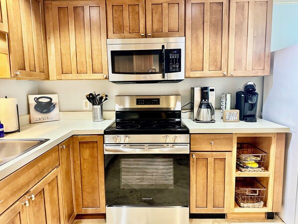 A kitchen with wooden cabinets, a stainless steel microwave, a stove, and a coffee maker.