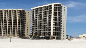 Un edificio de gran altura con varios pisos, balcones y una playa arenosa al frente.
