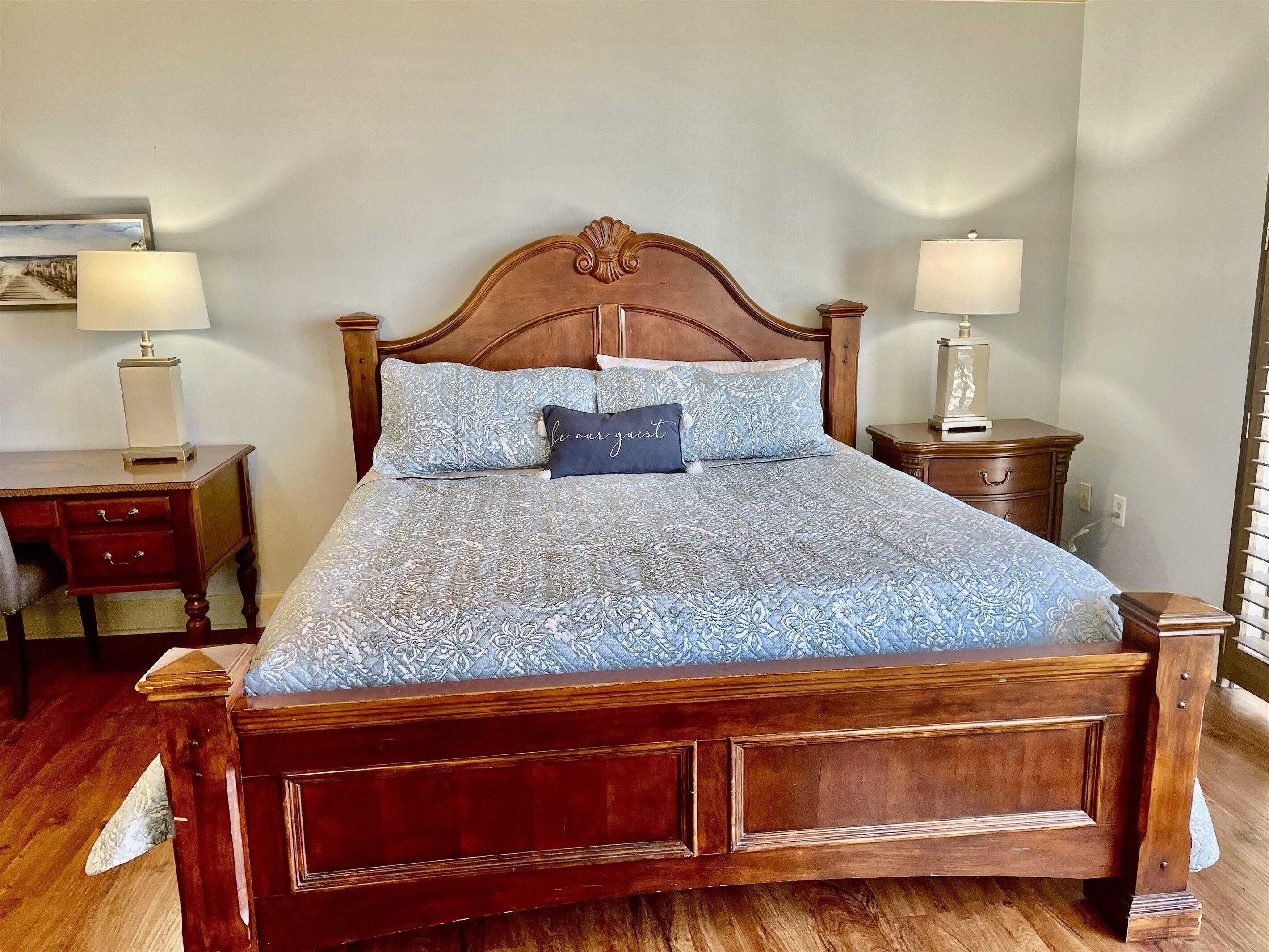 A wooden bed with a floral-patterned bedspread and two matching pillows, flanked by nightstands with lamps.