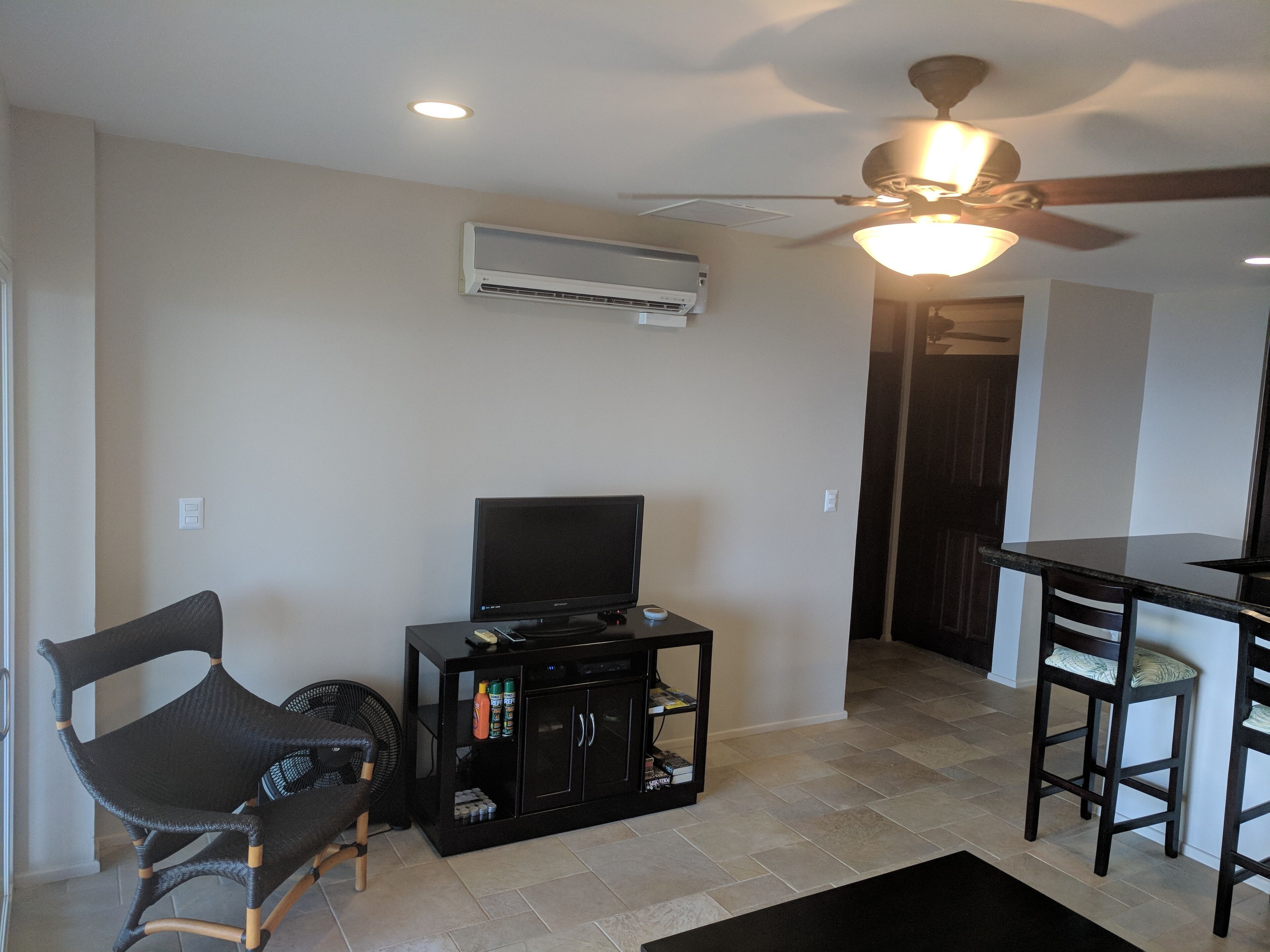 A living room with a ceiling fan, a flat-screen TV, a black entertainment unit, and a dining area with two chairs.