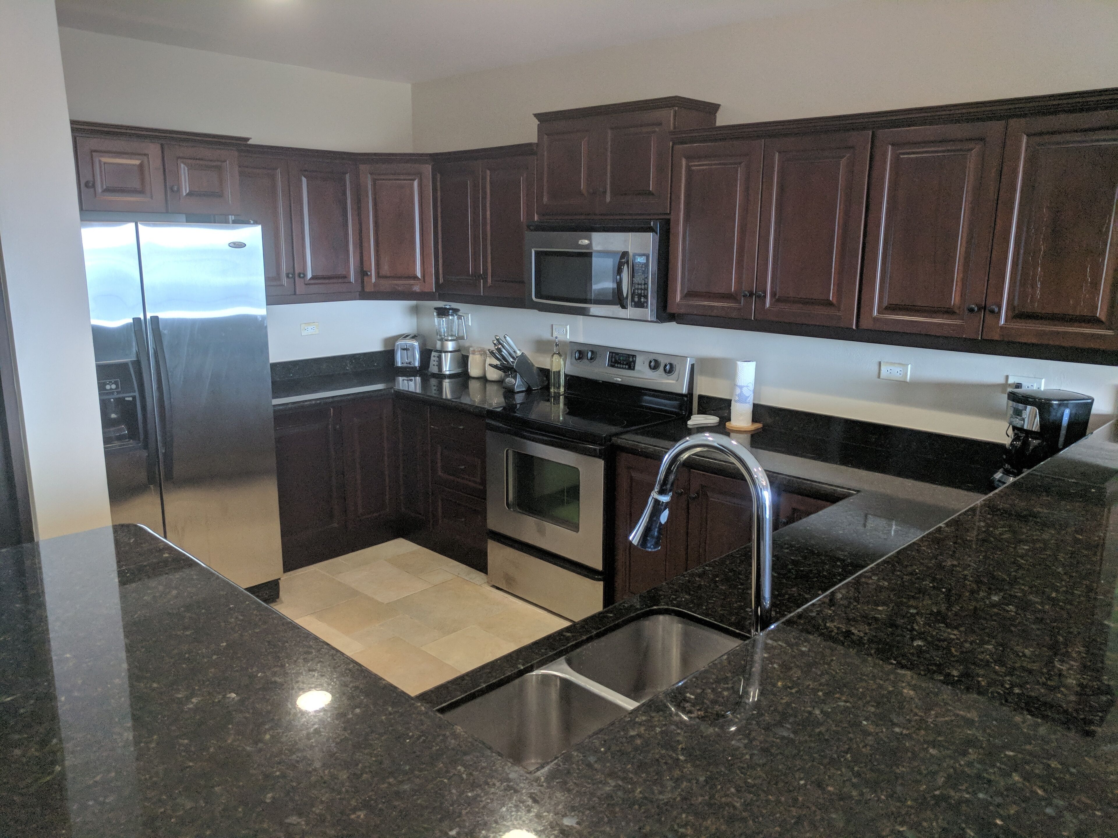 A modern kitchen with dark wooden cabinets, stainless steel appliances, and a granite countertop.