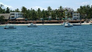 Un hotel frente al mar con vista a la playa, varias embarcaciones en el agua y palmeras.