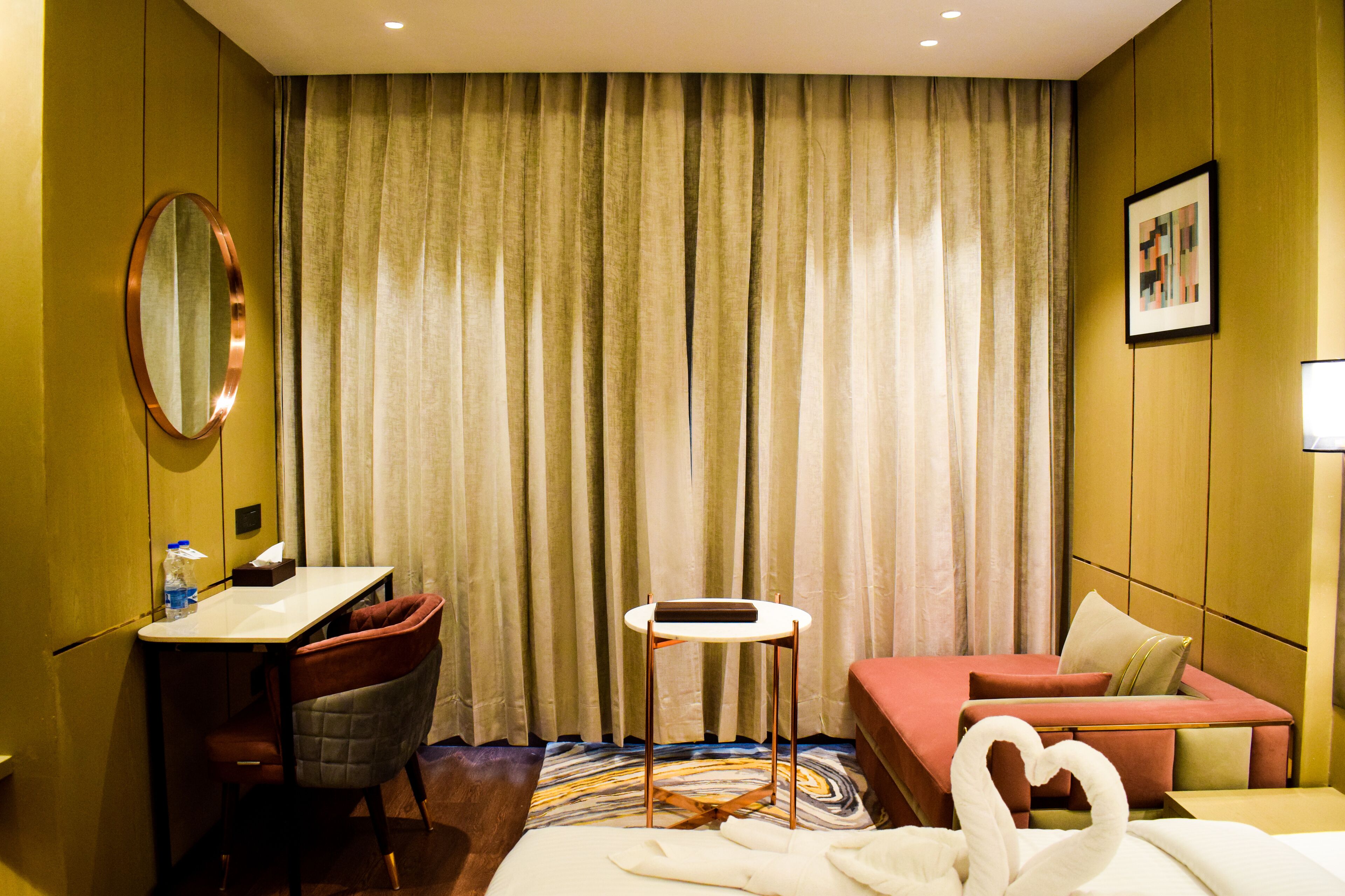 A hotel room with a bed, a desk, a chair, a small table, and a mirror.
