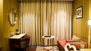 A hotel room with a bed, a desk, a chair, a small table, and a mirror.