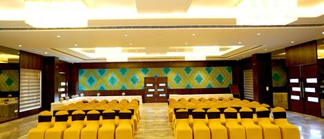 A conference room with rows of yellow chairs and a stage.