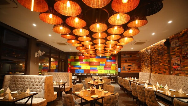 Un restaurant doté de nombreuses tables et de coins repas, d’un éclairage chaleureux et d’une décoration murale colorée.