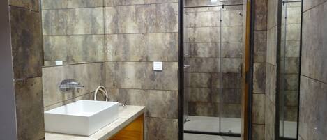 A modern bathroom with a large mirror, a white sink, and a glass-enclosed shower.