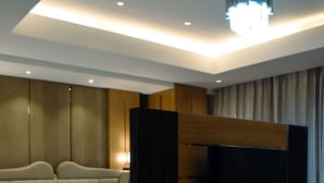 Une chambre d’hôtel moderne dotée d’un grand lit, d’un téléviseur à écran plat fixé sur un panneau en bois, d’une table basse ronde et d’un luminaire au plafond.