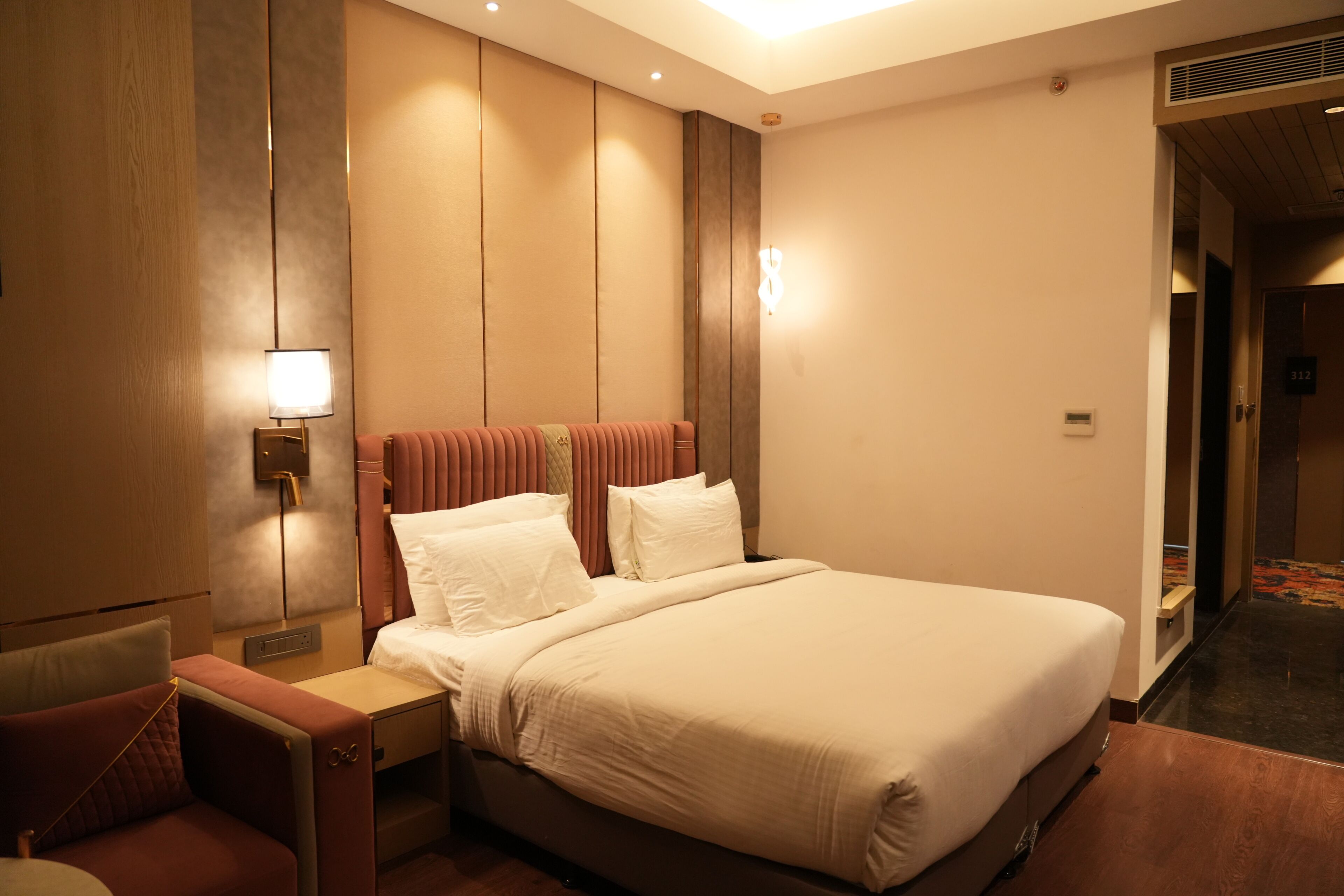 A hotel room with a large bed, a bedside table, a lamp, and a door to the hallway.