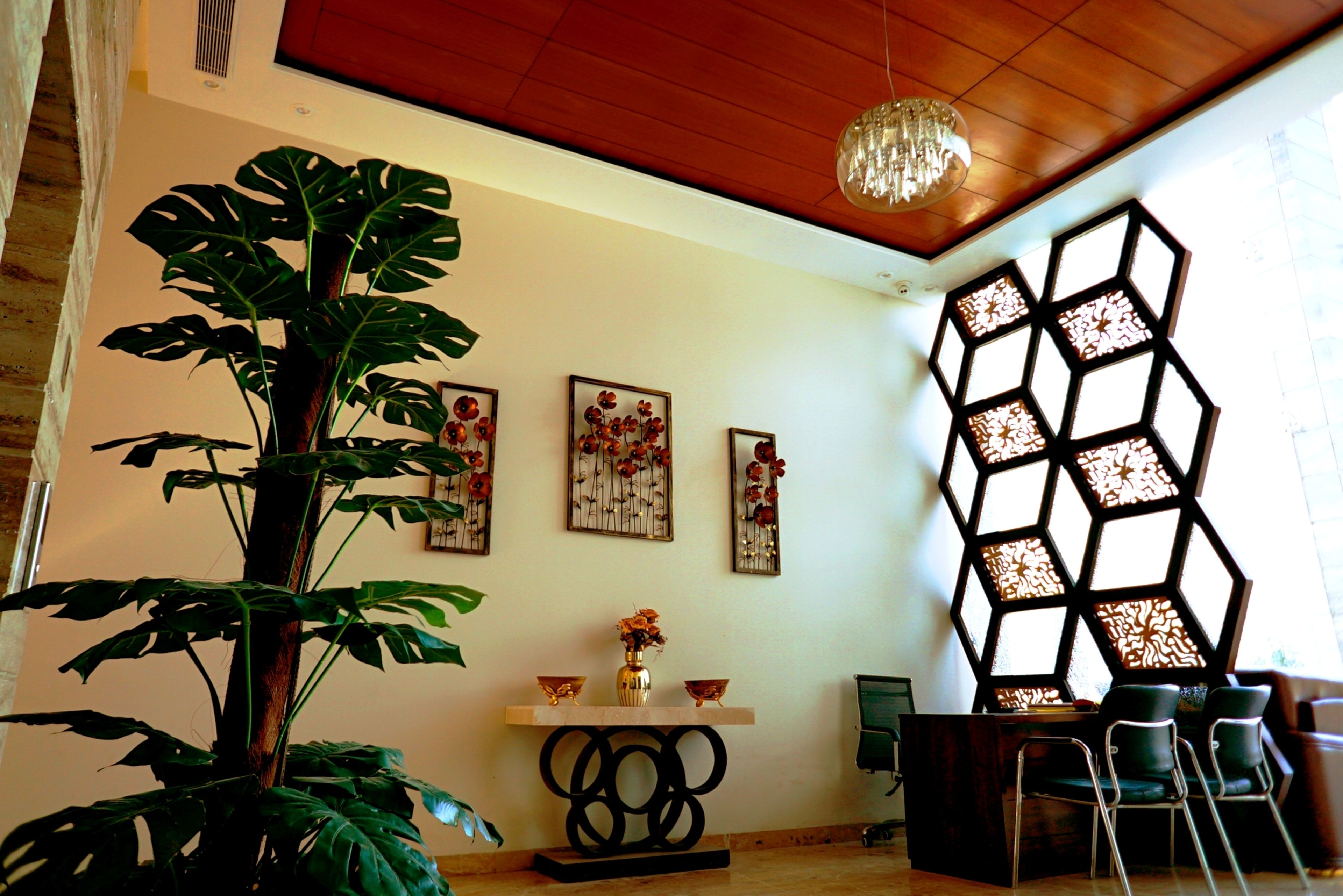 Et værelse med en stor plante, træloft, en lysekrone, en væg med hexagonpaneler og et spiseområde med stole og et bord.