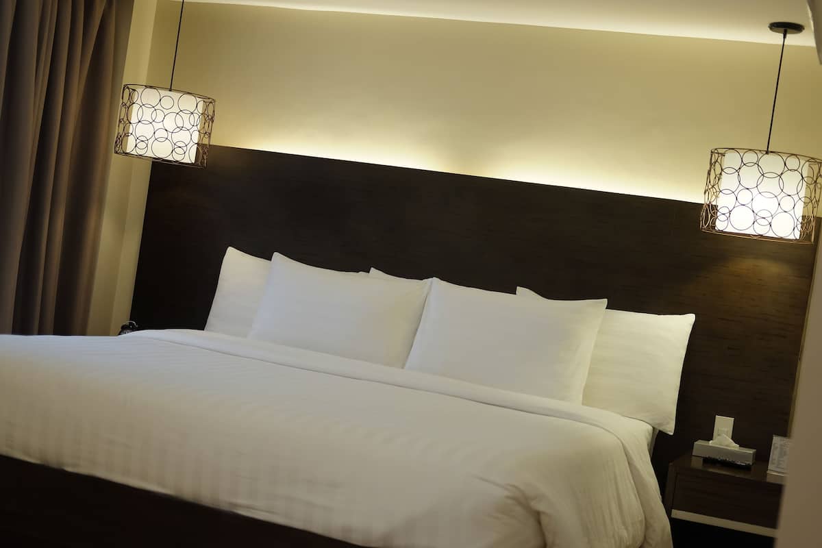 A neatly made bed with white linens and a dark headboard. There are two bedside tables, one with a tissue box and a small item on it.