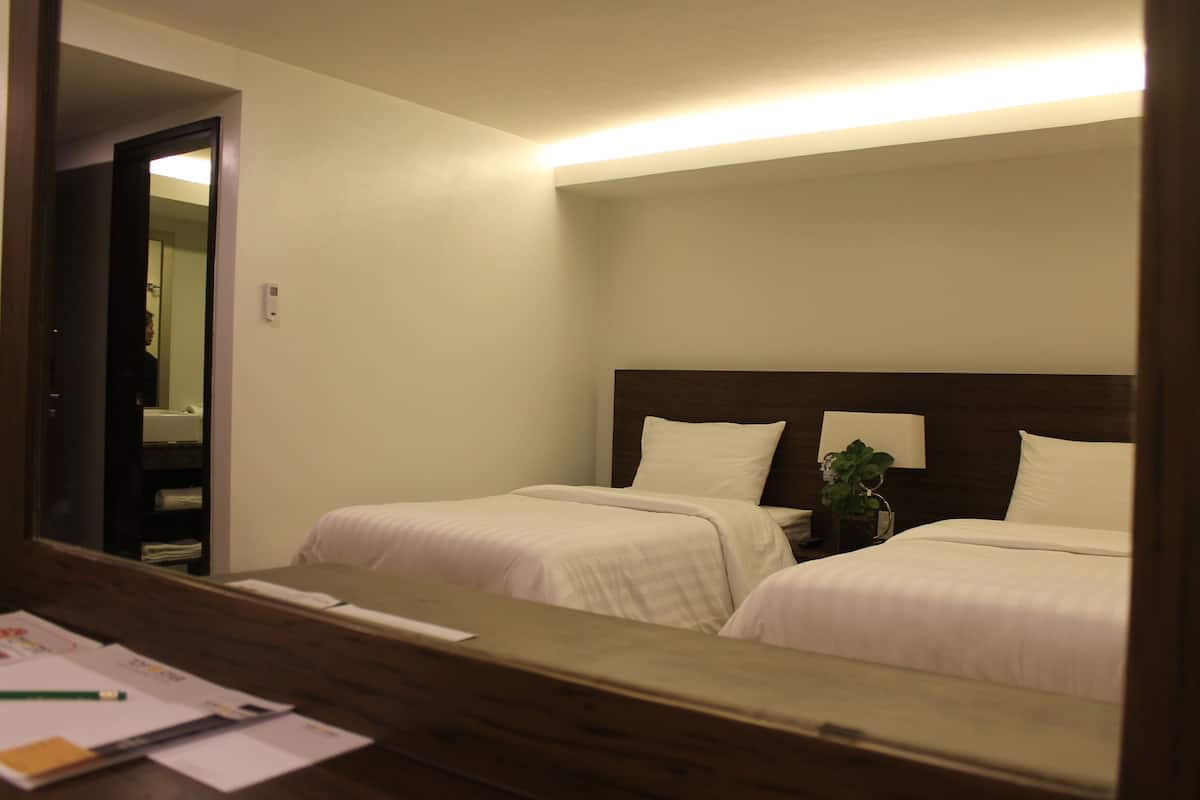 A hotel room with two beds, a wooden desk, a mirror, and a nightstand with a lamp and a plant.