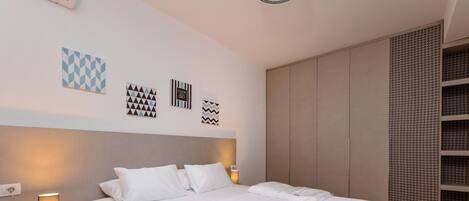 A modern bedroom with a large bed, bedside lamps, and a wardrobe.
