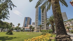 A tall building with multiple floors, surrounded by greenery and palm trees. - Apartments Krug (Budva)