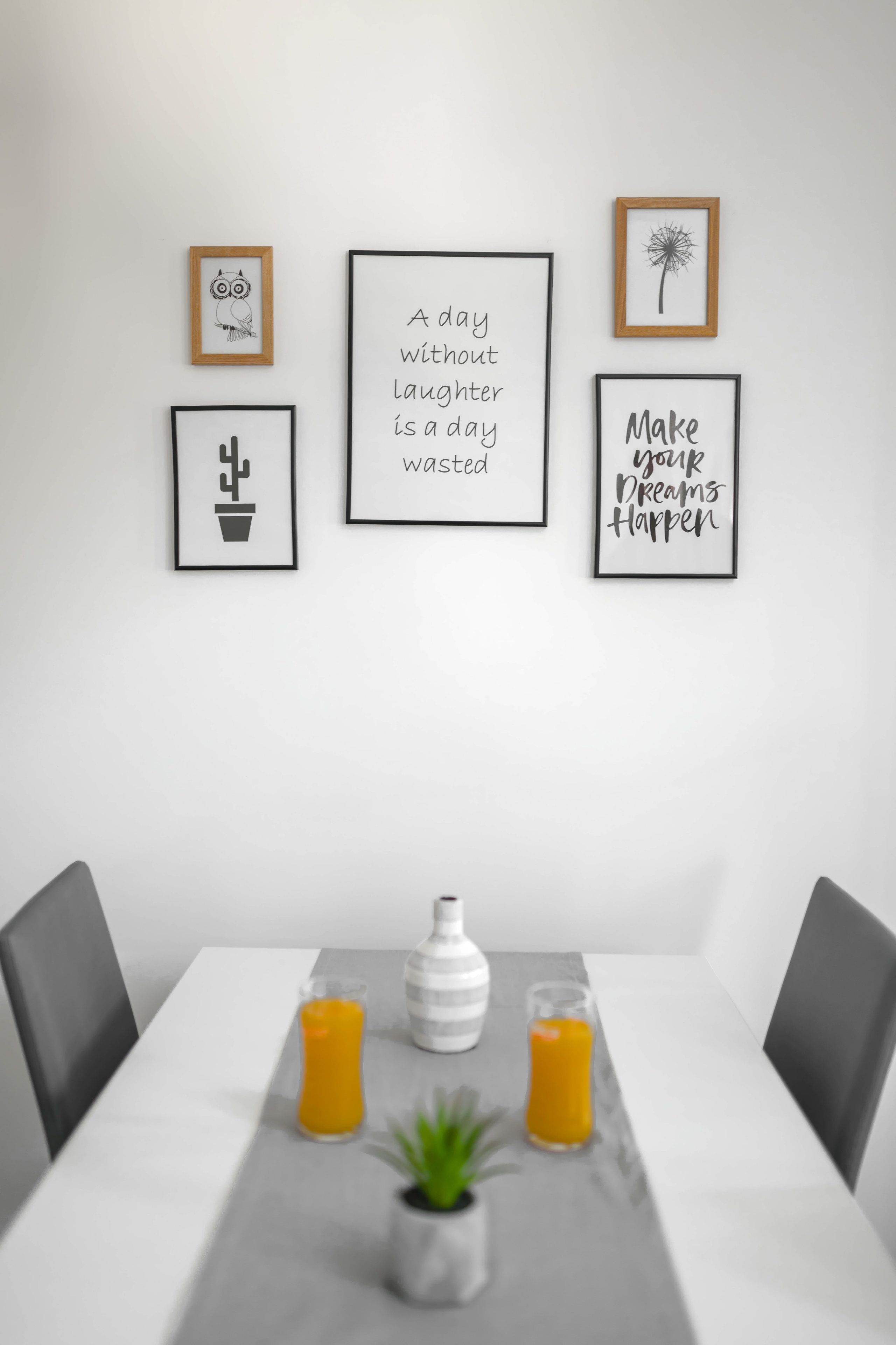 Een eetgedeelte met een witte tafel, twee stoelen, een bloempot en twee glazen sinaasappelsap.