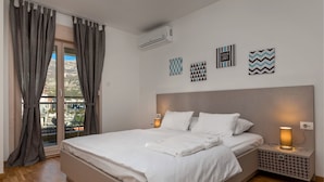 A bedroom with a bed, nightstands, an air conditioner, and decorative wall art. - Apartments Krug (Budva)