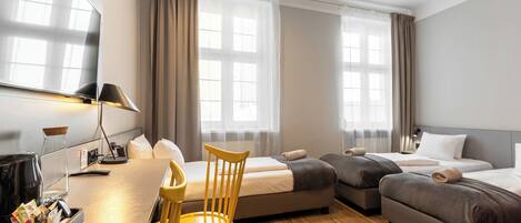 A hotel room with a desk, two beds, a chair, and a TV.