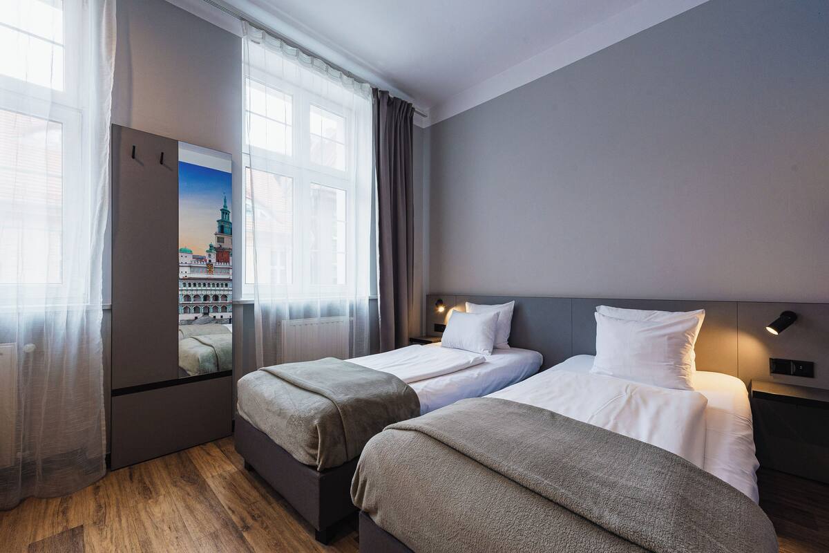 Habitación de hotel con dos camas individuales, un ventanal grande con cortinas y vistas a la ciudad, con un diseño moderno.